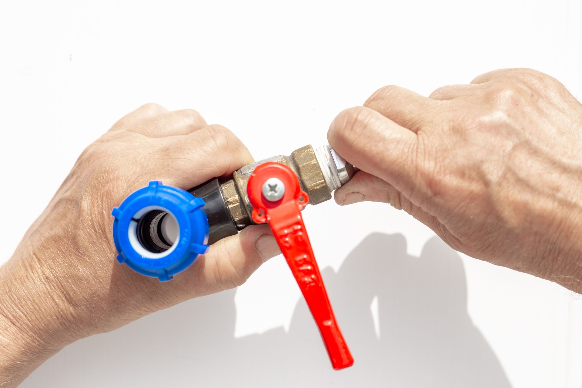 Close-up of hands assembling metal threaded faucet part with blue plastic fittings and red valve