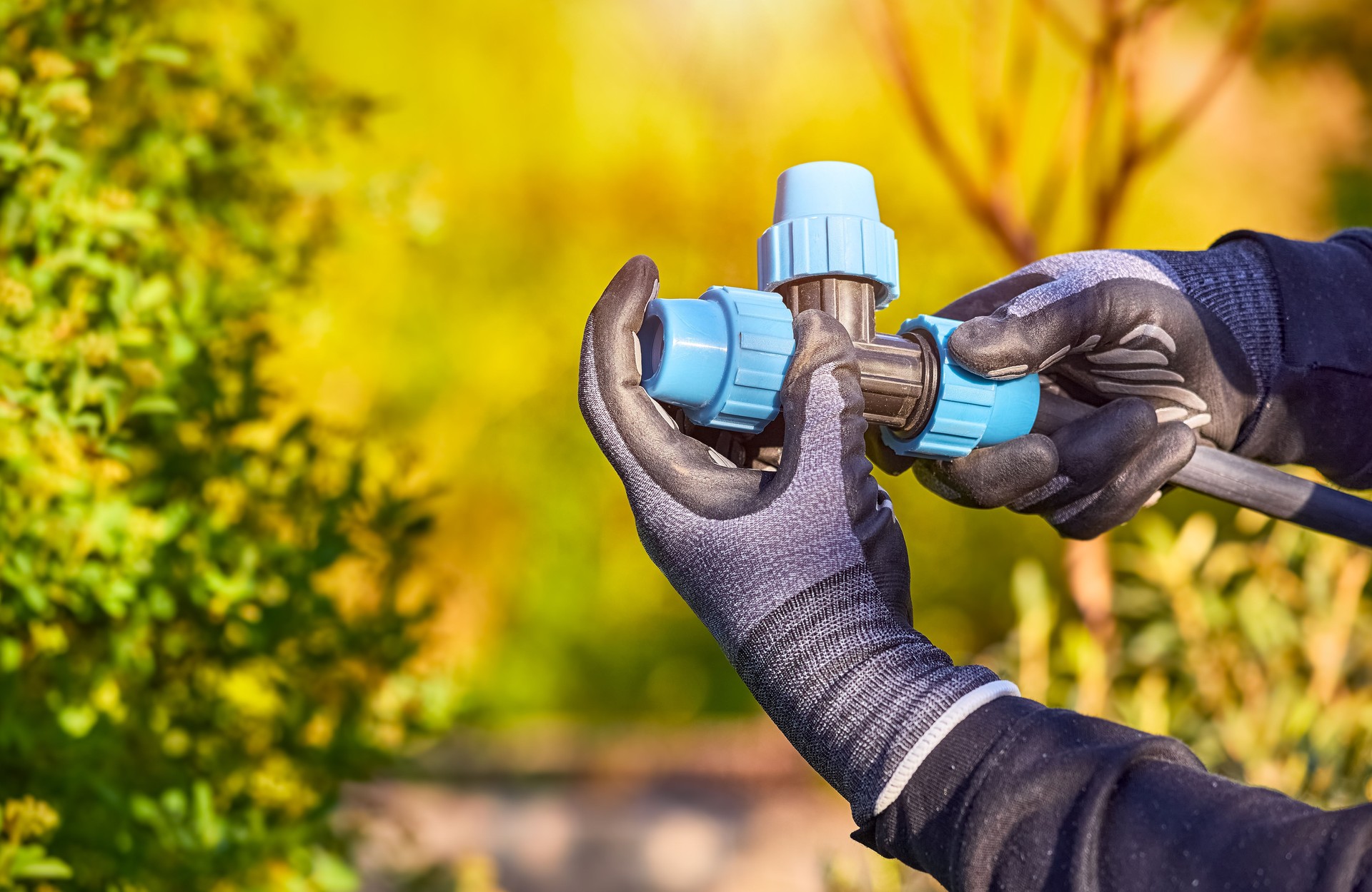 Closeup of hands in the gloves. Process of installing fittings pipes and connectors for the garden and lawn irrigation system installation. Green during sunset, shallow depth of field.